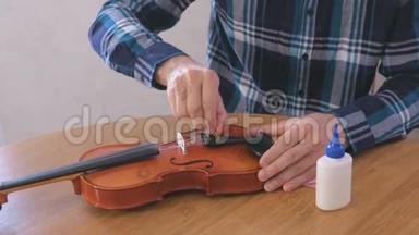 穿格子衬衫的年轻人的特写<strong>双手</strong>正在修理<strong>坐</strong>在桌子旁的小提琴。